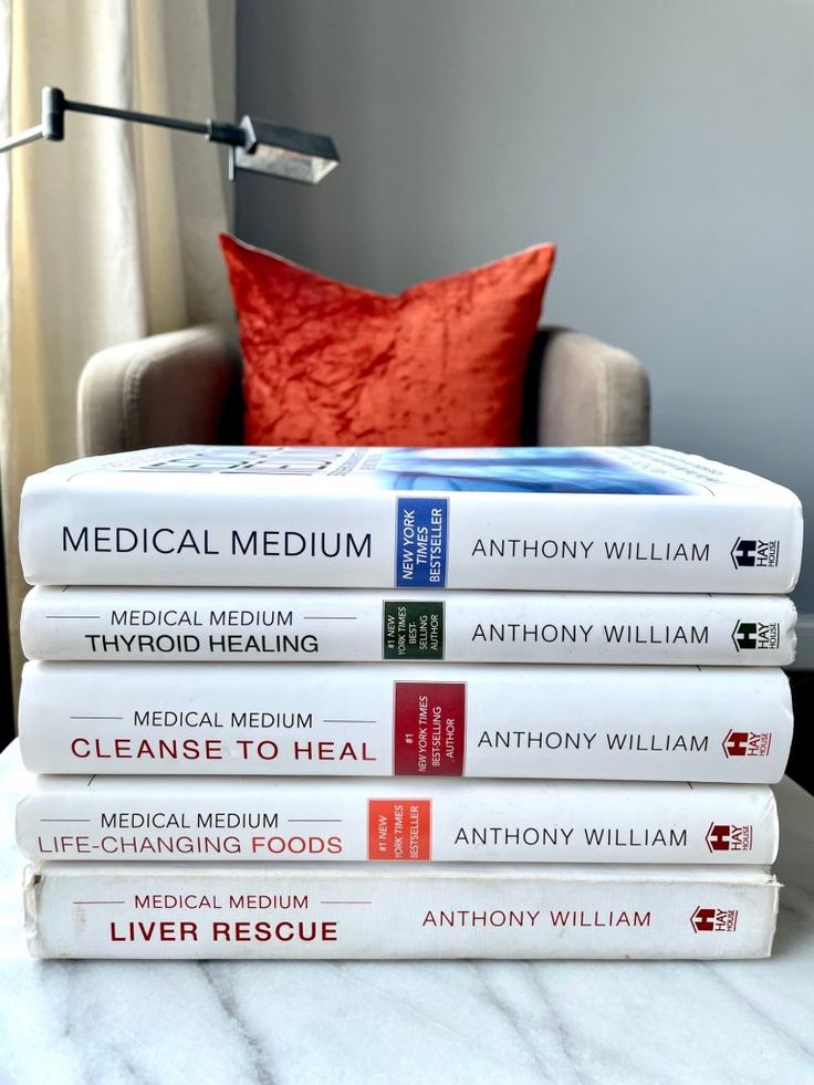 a stack of medical books sitting on top of a table next to a chair and lamp