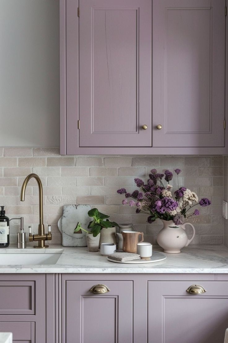 a kitchen with purple cabinets and white counter tops, gold faucets and vases on the sink