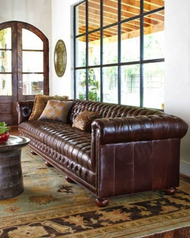 a brown leather couch sitting in front of a window with lots of pillows on it