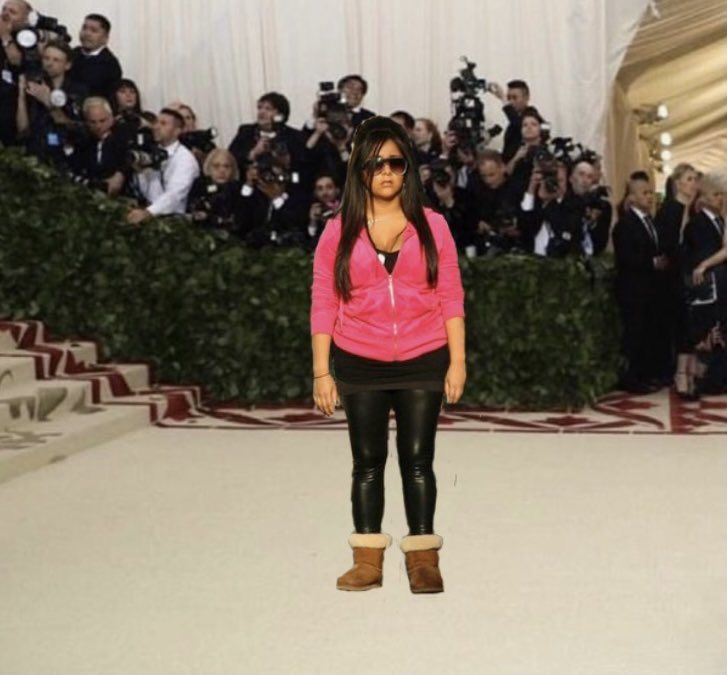 a woman in pink jacket and black pants standing on white carpet with people behind her