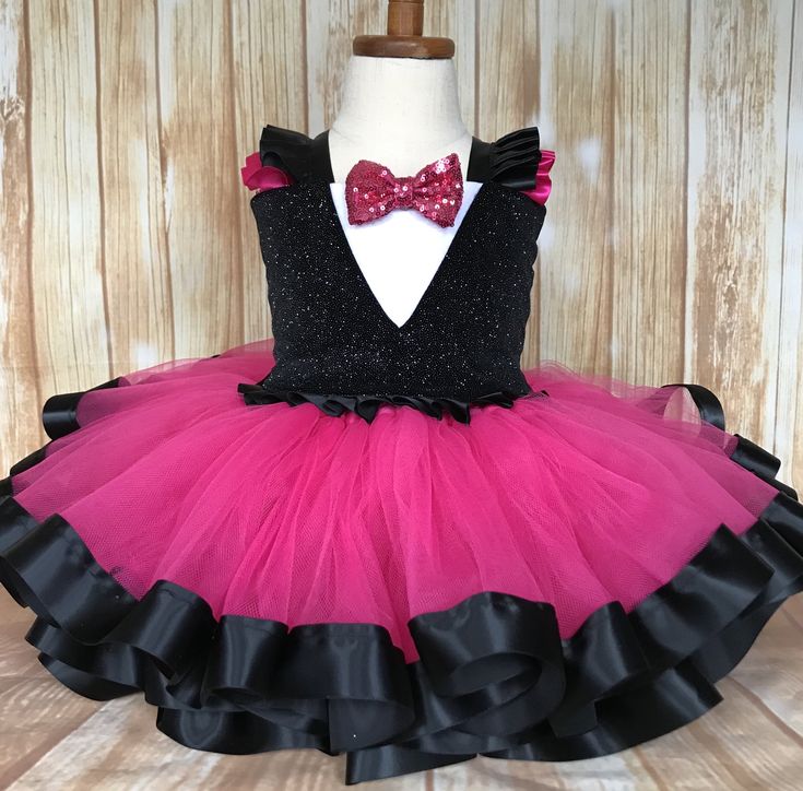 a pink and black tutule dress with a red bow on the top, sitting on a mannequin