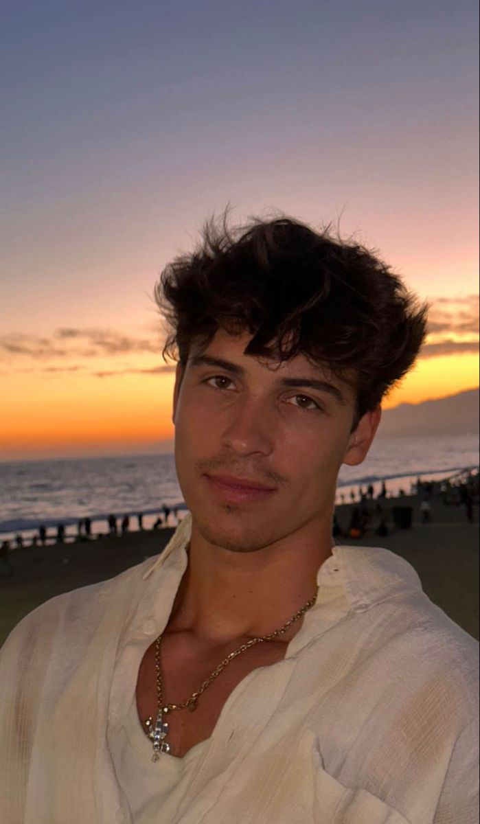 a man standing on top of a sandy beach next to the ocean at sunset with people in the background