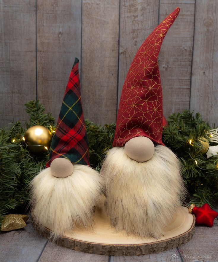 two gnomes sitting on top of a wooden table next to christmas decorations and greenery