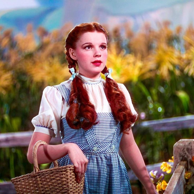 a woman with long red hair holding a wicker basket in front of some flowers