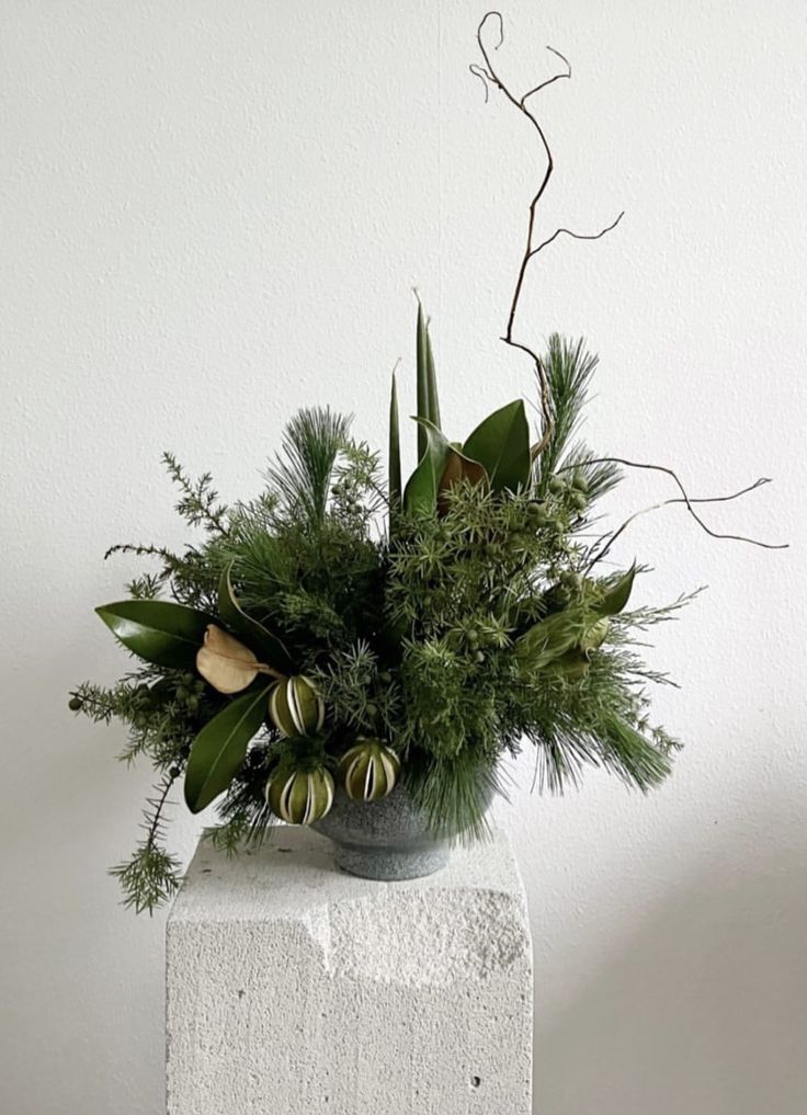 a vase filled with greenery sitting on top of a white block next to a wall