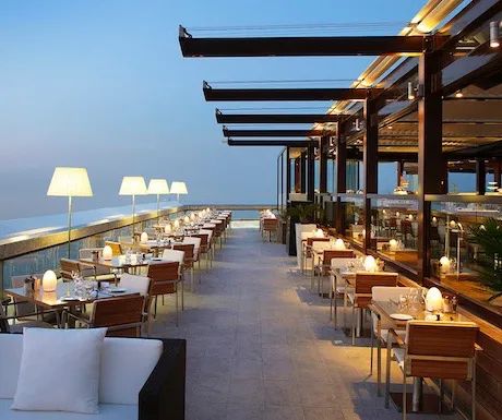 an outdoor dining area overlooking the ocean at dusk with tables and chairs set up for dinner