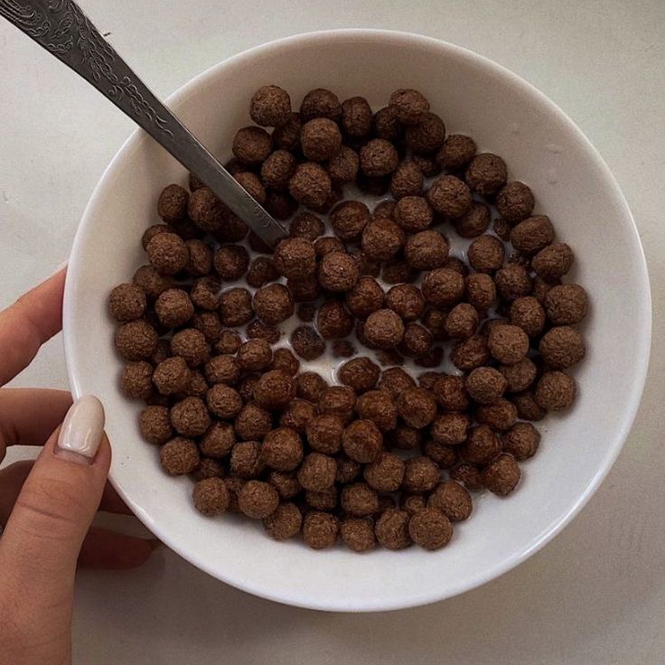 a person is holding a spoon over a bowl of chocolate truffles on a table