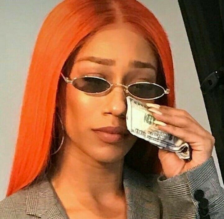 a woman with orange hair and sunglasses talking on a cell phone while holding money in front of her face