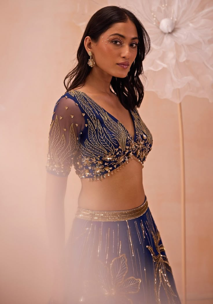 This exquisite Blue Embellished Lehenga set, crafted from delicate net fabric, perfectly blends traditional charm and contemporary elegance. The blue lehenga is heavily embellished with large, intricate floral motifs and linear designs, created using a stunning combination of zari, sequins, beads, and cutdana work. The richly adorned skirt is paired with a matching blouse that features complementary embroidery, adding to the overall opulence of the ensemble. The sheer dupatta drapes gracefully, Fitted Blue Pre-draped Saree With Intricate Embroidery, Blue Palazzo Set With Sheer Dupatta For Reception, Blue Embellished Sharara For Reception, Party Blue Pre-draped Saree With Intricate Embroidery, Blue Embellished Georgette Lehenga, Elegant Blue Embellished Lehenga, Embellished Blue Sets For Reception, Embellished Blue Anarkali Pre-draped Saree, Blue Party Wear Choli For Festive Occasions