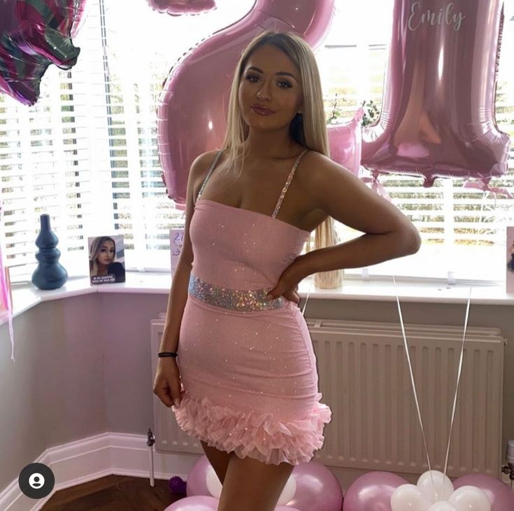 a woman in a pink dress posing for the camera with balloons and heliums behind her