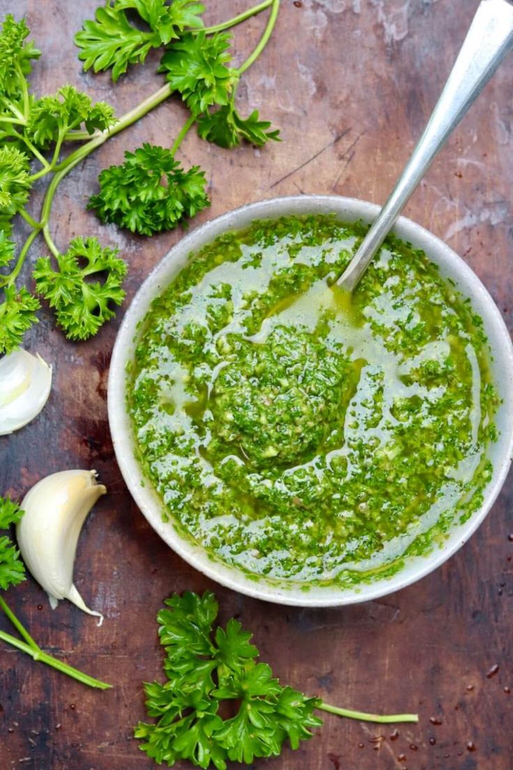 a bowl filled with pesto next to garlic and parsley