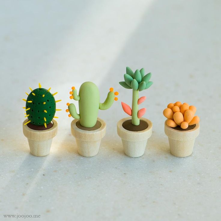 three small cactus plants in wooden pots on a white countertop, one is green and the other is orange