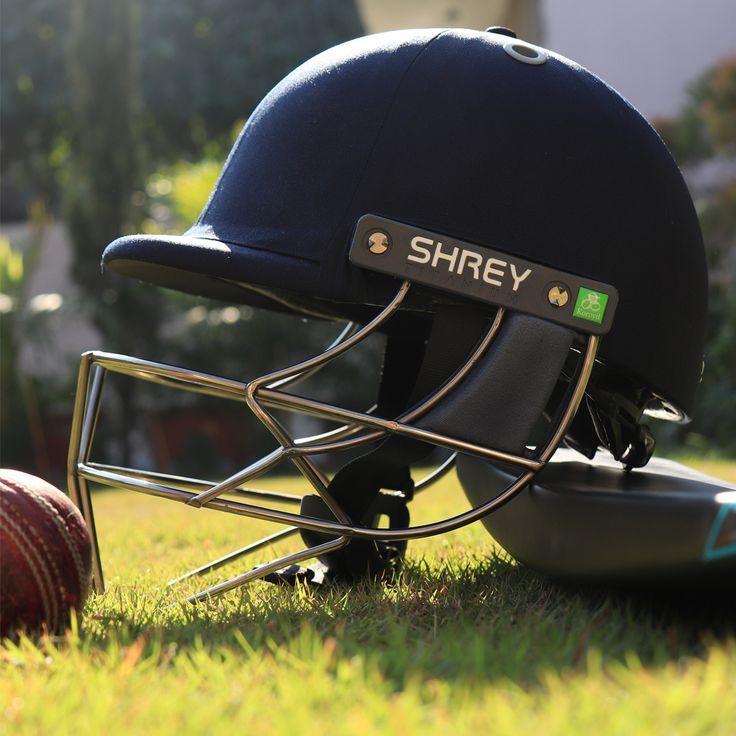 a helmet sitting on the ground next to a cricket ball