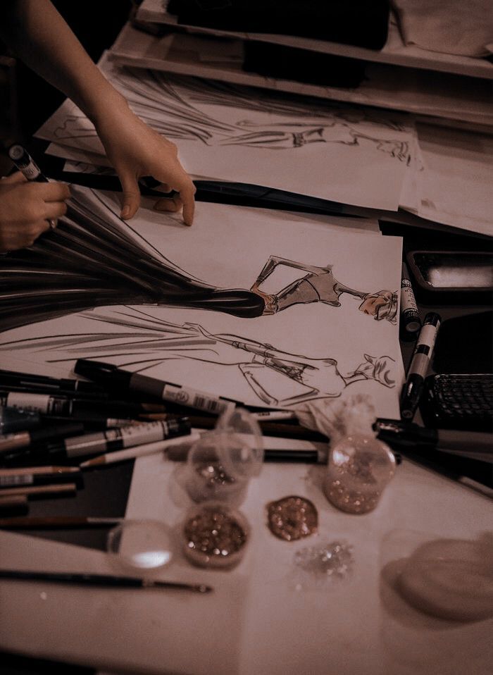 the woman is drawing on paper with her hands and other art supplies around her table