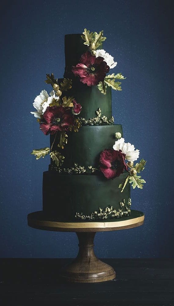 a three tiered green cake with flowers on the top and bottom, against a blue background