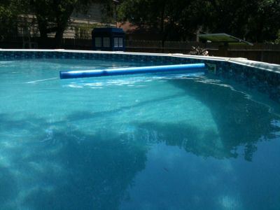 an empty swimming pool with blue water and trees in the backgroung area