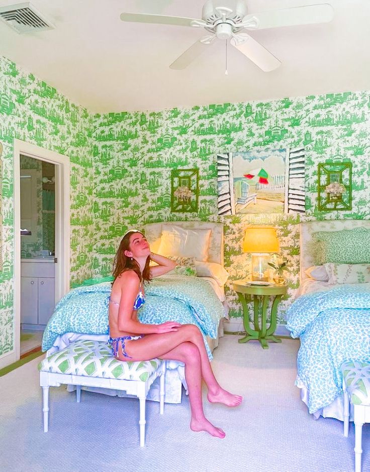 a woman sitting on a bed in a room with green and white wallpapers