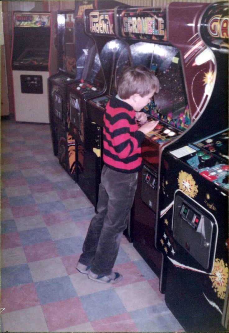 a young boy standing in front of an arcade machine