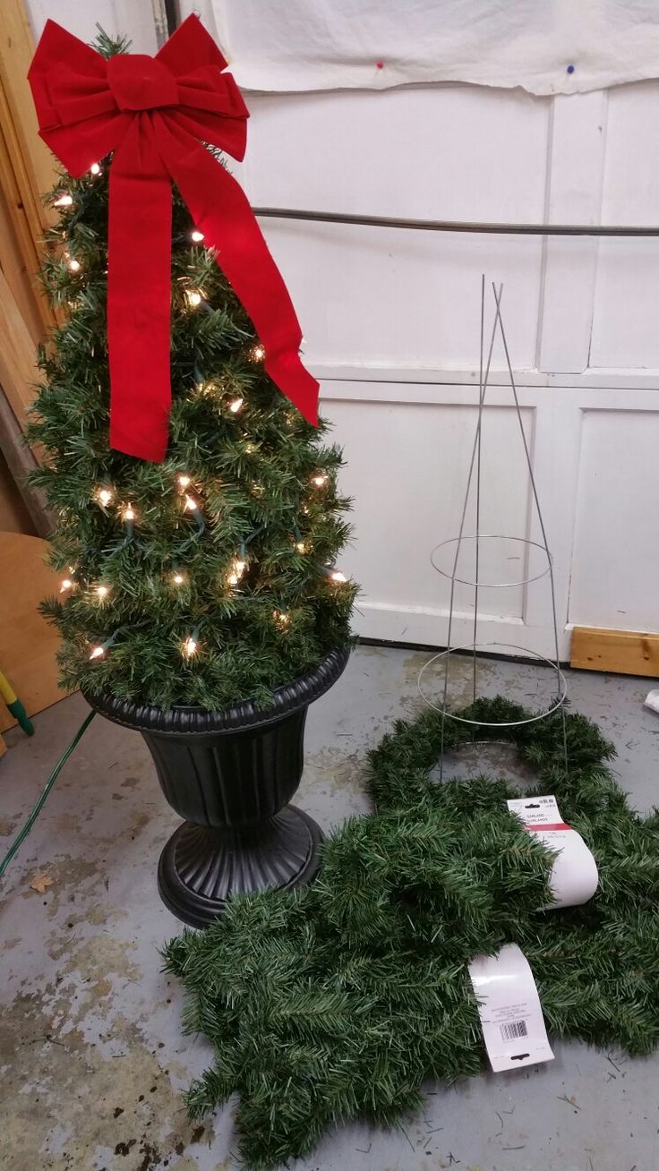 a small christmas tree sitting on the ground next to a potted plant with red ribbon