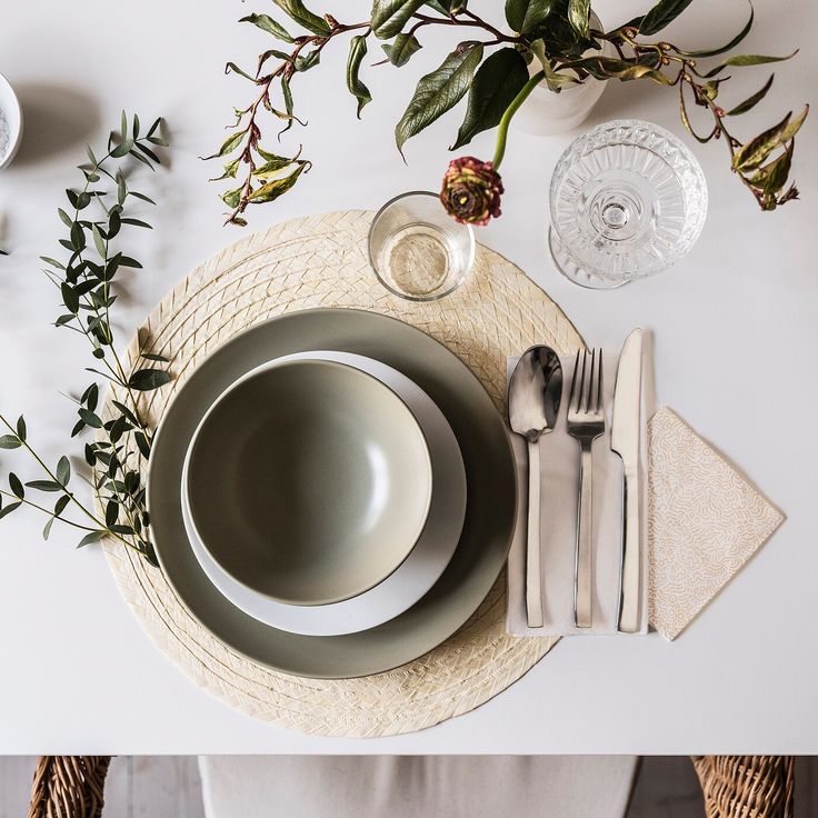 a place setting with plates, silverware and greenery on the table for two