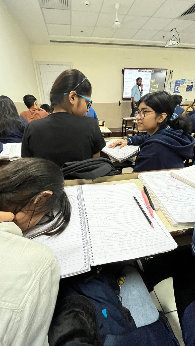 several students are sitting at desks with notebooks and papers in front of them