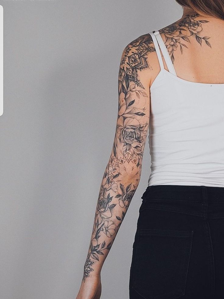 a woman with tattoos standing in front of a white wall and looking at the camera