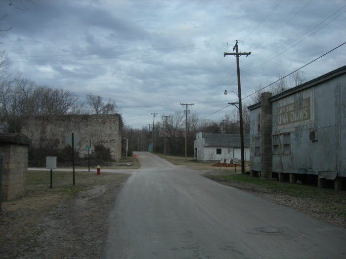 an empty dirt road in front of some buildings and telephone poles on the other side