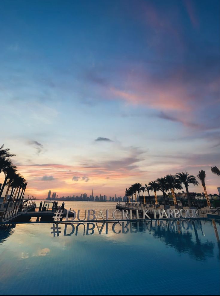 an empty swimming pool with palm trees and the ocean in the background at sunset or dawn