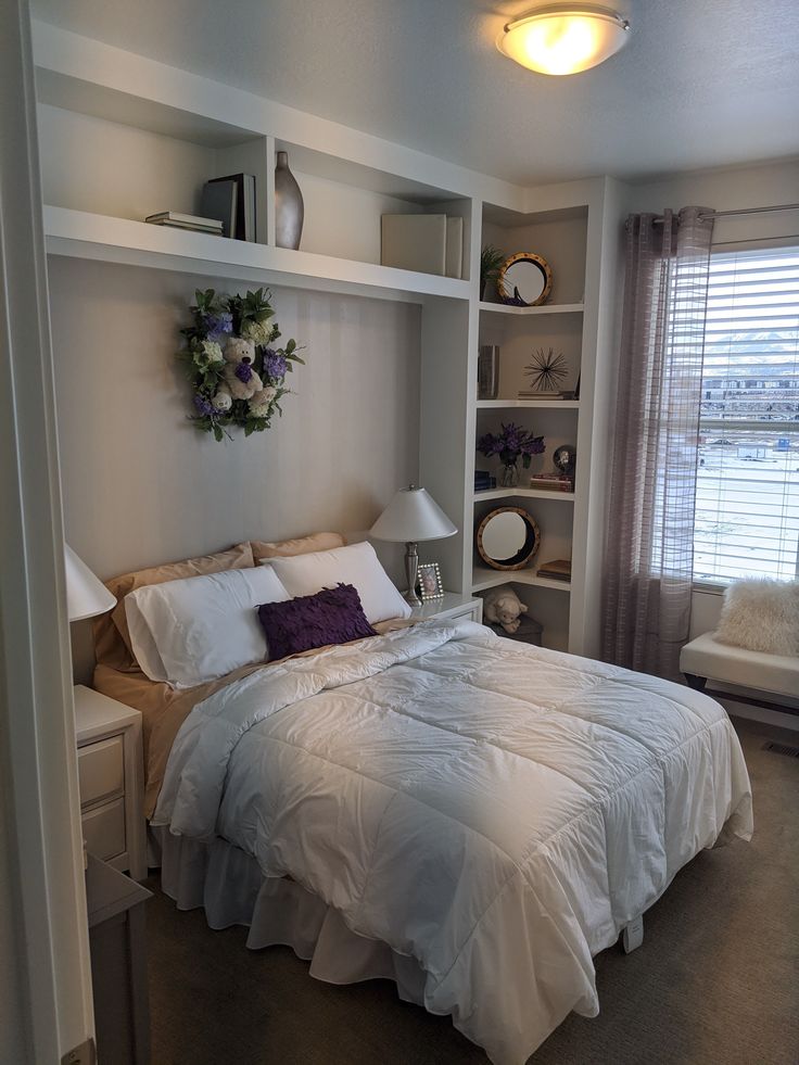 a bed with white sheets and pillows in a bedroom next to a book shelf filled with books