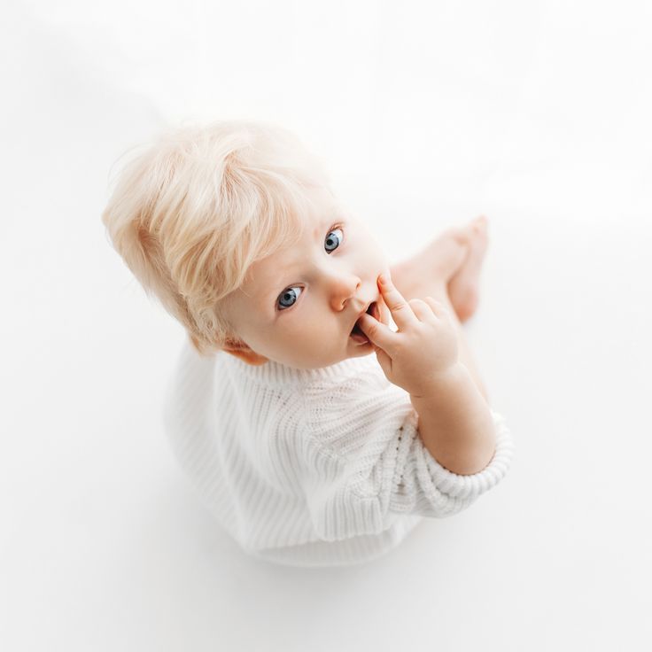 a baby is sitting on the floor with his hands in his mouth and looking at the camera