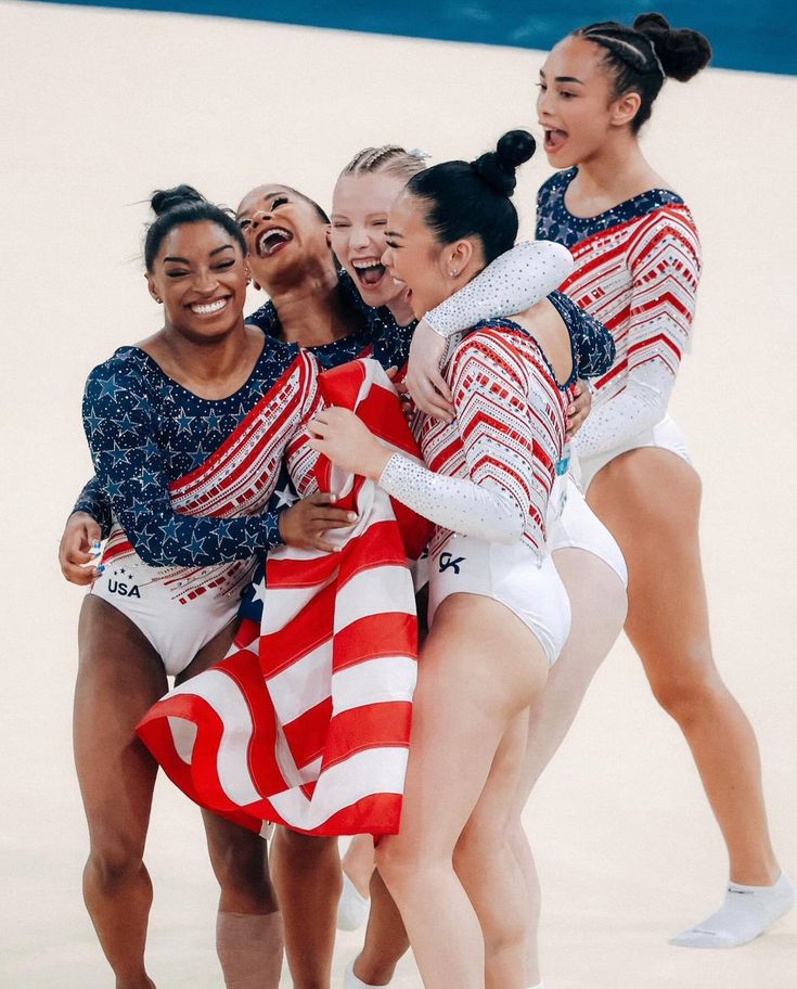 four female olympic figure skaters hugging each other in front of an american flag on the ice