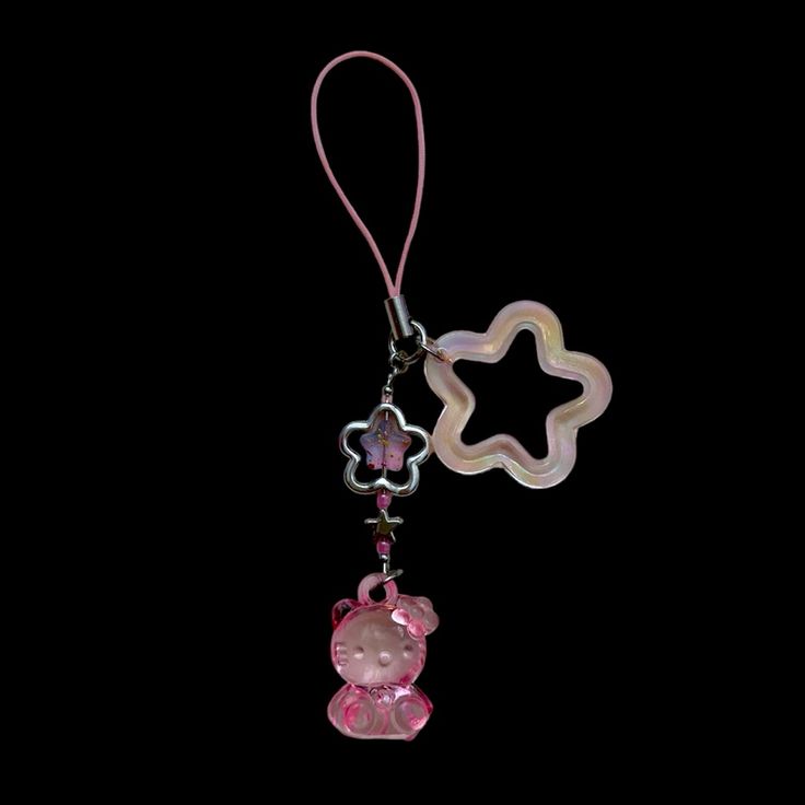 a pink teddy bear charm hanging from a string on a black background with a star shaped object attached to it