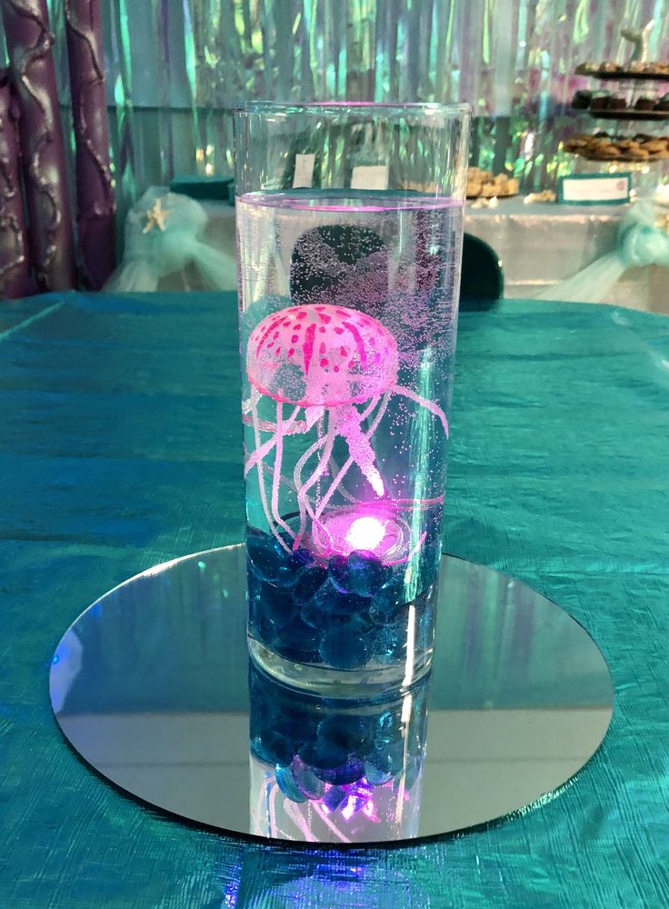 a glass filled with water and jellyfish on top of a blue cloth covered table