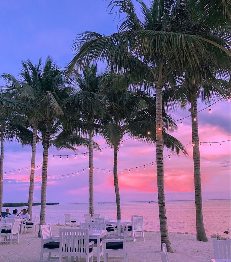 palm trees line the beach at sunset with tables and chairs set up for an event