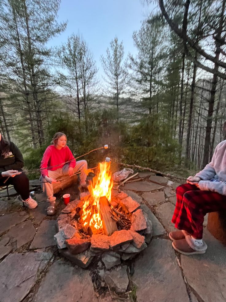 three people sitting around a campfire in the woods