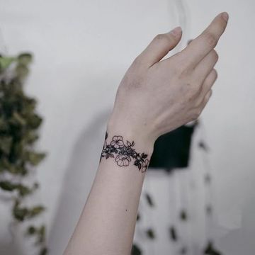 a woman's arm with a black flower tattoo on her left wrist and the other hand