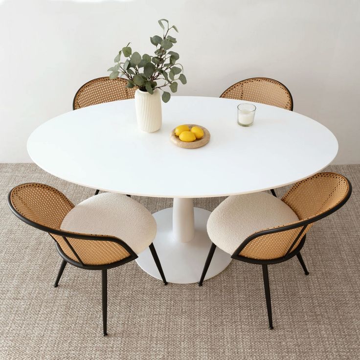 a white table with four chairs and a vase filled with lemons on the top