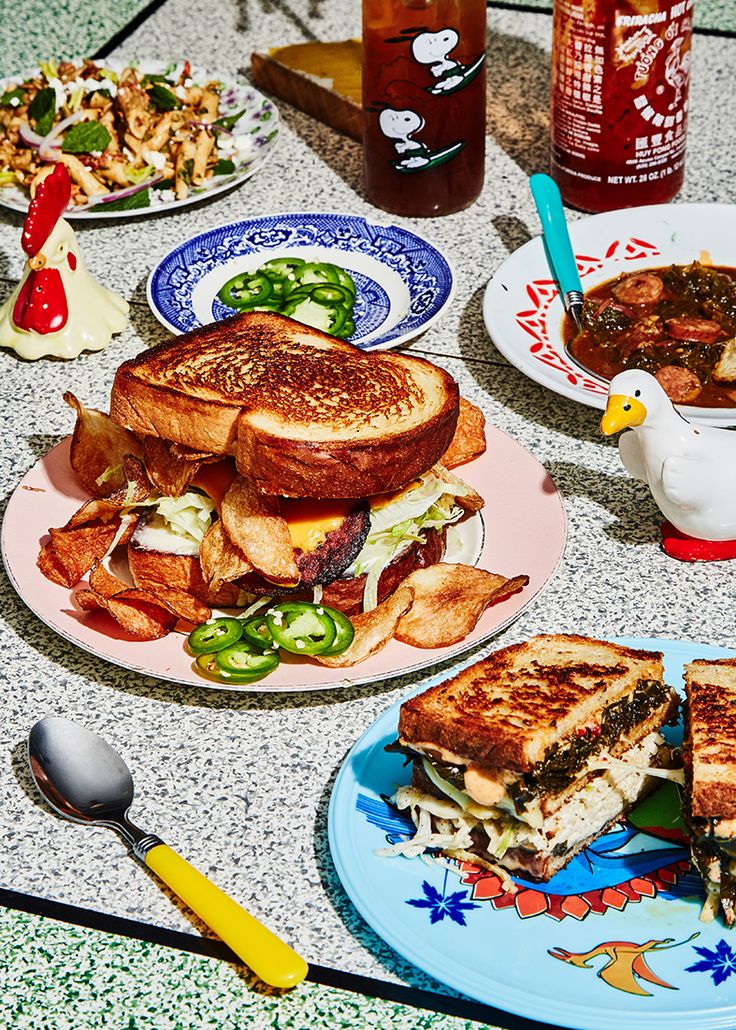 a table topped with plates filled with sandwiches and bowls of food next to cups of soup