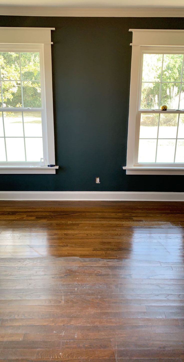 an empty room with two windows and hard wood flooring in the foreground is a blue painted wall