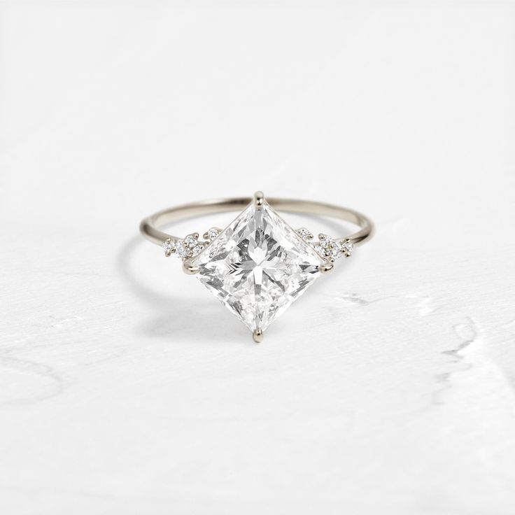 a white gold ring with a princess cut diamond and three small diamonds on the side