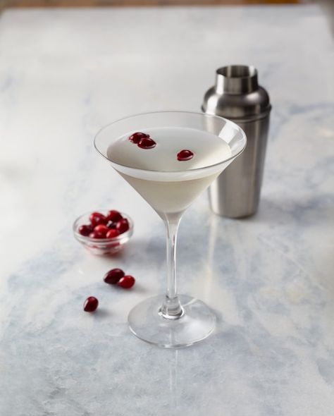 a martini with cranberries in it and a cocktail shaker next to it