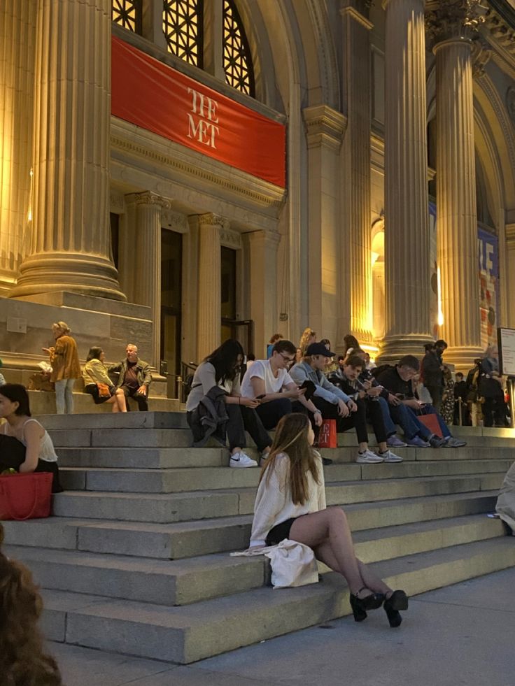 many people are sitting on the steps in front of a building with columns and pillars