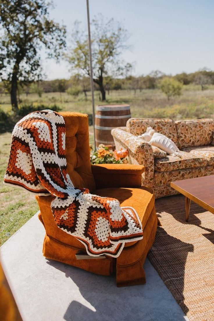 an orange chair with a crocheted blanket on it sitting in front of a couch