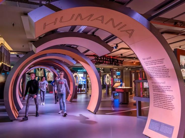 three people are walking through an exhibit with pink arches and signs on the walls that read, humania