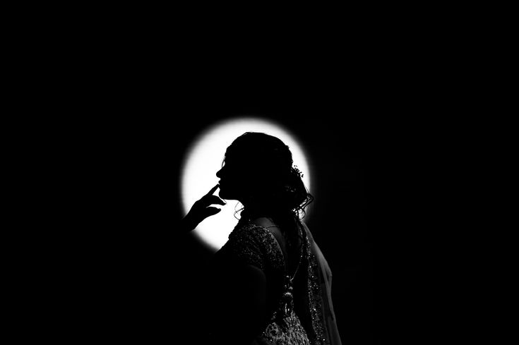 a woman standing in the dark holding her hand to her face and looking at the moon