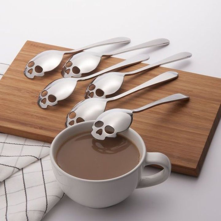 six spoons with skulls on them are sitting next to a cup of hot chocolate