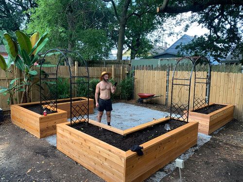 a man standing in the middle of two raised beds with dirt on top and plants growing out of them