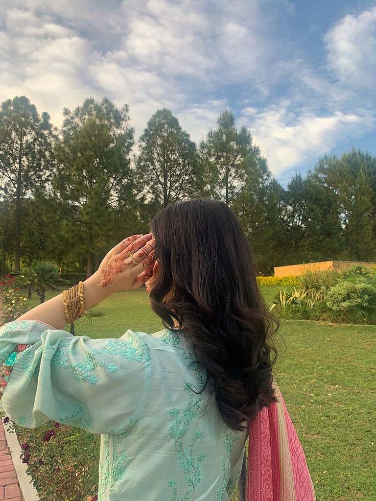 a woman standing on top of a lush green field holding her hands up to her face