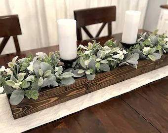 a wooden table topped with candles and greenery