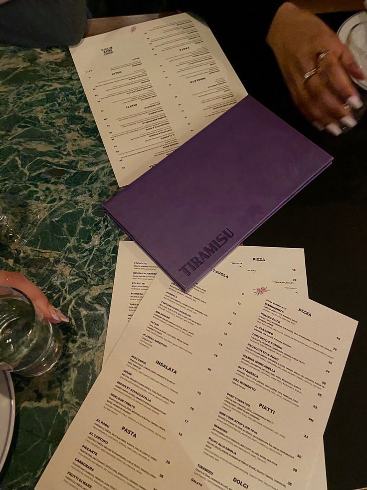 two people sitting at a table with menus and wine glasses on top of it